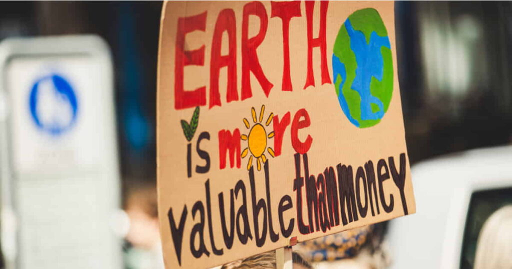 Uncovering AI's Dirty Environmental Impact-cardboard sign says" Earath is more valuable than money"